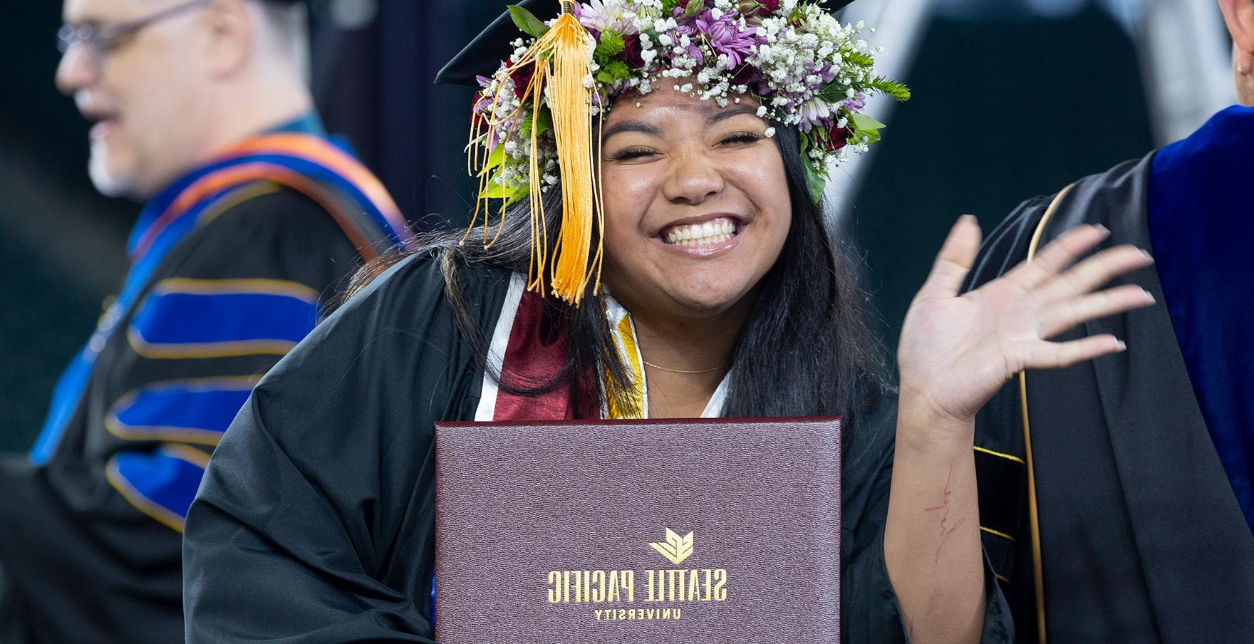 An SPU student smiles and waves with her diploma | photo by Mike Siegel